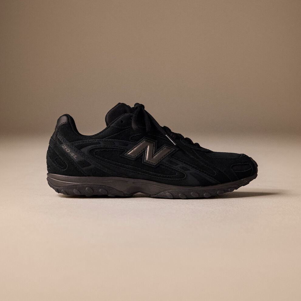Side image of a black 204L sneaker on a brown background